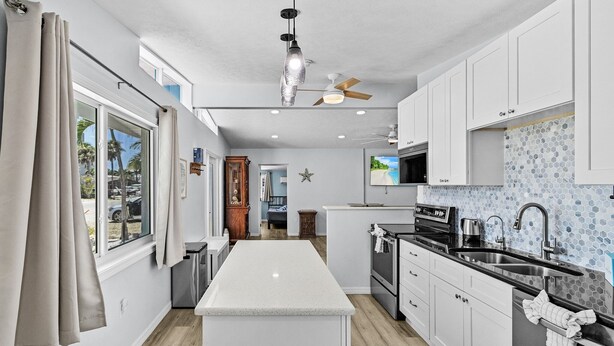 Une cuisine moderne avec des meubles blancs, un îlot central, un plan de travail noir et un revêtement mural en carreaux.