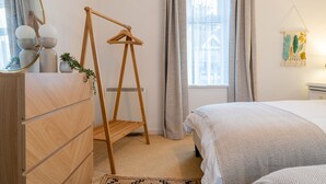 Une chambre à coucher avec un lit, une commode en bois, un étendoir en bois et une fenêtre avec des rideaux.