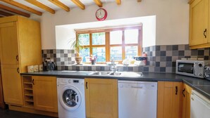 Une cuisine avec des meubles en bois, un lave-linge, un lave-vaisselle, un four à micro-ondes et une fenêtre donnant sur un paysage verdoyant.
