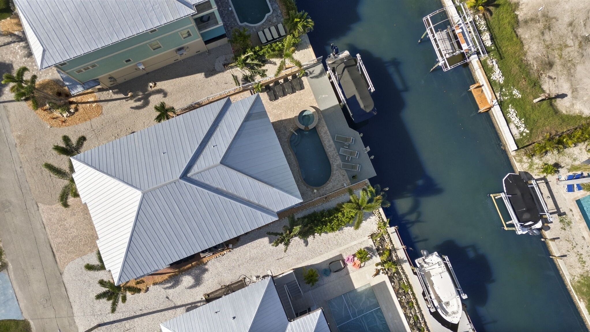 Una propiedad costera con una piscina grande, un muelle con barcos y un edificio de techo inclinado.