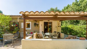 A covered patio area with outdoor seating, a door leading to a room, and a garden with potted plants.