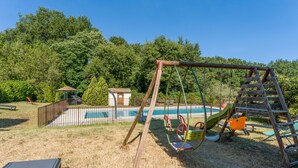 A backyard with a swing set, a small pool, and a fenced area.