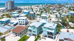 A coastal residential area with multiple two-story houses, a prominent tall building, and a clear view of the ocean.