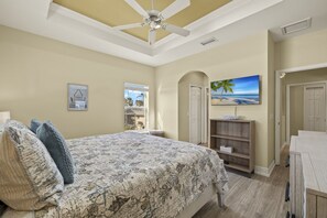 A bedroom with a bed, a ceiling fan, a painting, and a view of the beach through a window. - 241 Oasis Pearl: 3br Pool Home! 3 Bedroom Home (Fort Myers Beach)