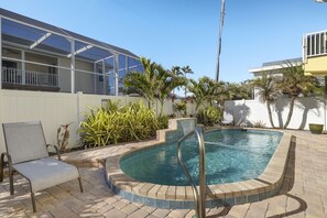 A swimming pool with a metal ladder, surrounded by a brick patio and palm trees.