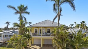 A yellow two-story house with a balcony, surrounded by palm trees and a clear blue sky. - 241 Oasis Pearl: 3br Pool Home! 3 Bedroom Home (Fort Myers Beach)