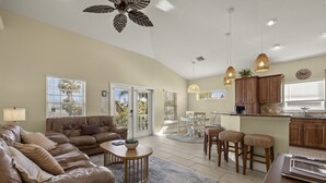 A spacious living area with a brown leather sofa, a round coffee table, and a dining area with a white table and chairs. - 241 Oasis Pearl: 3br Pool Home! 3 Bedroom Home (Fort Myers Beach)