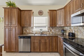 Una cocina con armarios de madera, lavavajillas de acero inoxidable, horno empotrado y microondas.