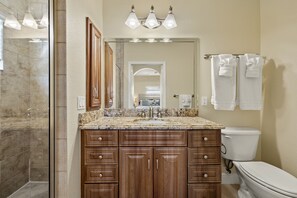 A bathroom with a marble sink, wooden cabinets, a toilet, and a glass shower enclosure. - 241 Oasis Pearl: 3br Pool Home! 3 Bedroom Home (Fort Myers Beach)
