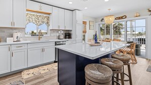 A modern kitchen with white cabinets, a large island, and bar stools. - 197 Beach Daze: 3br Pool Home, W/ Deeded Beach Access! 3 Bedroom Home (Fort Myers Beach)