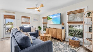 A modern living room with a large sofa, a wooden cabinet, a TV, and a ceiling fan. - 197 Beach Daze: 3br Pool Home, W/ Deeded Beach Access! 3 Bedroom Home (Fort Myers Beach)