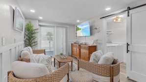 A living room with wicker furniture, a television, and a sliding door to the kitchen. - 197 Beach Daze: 3br Pool Home, W/ Deeded Beach Access! 3 Bedroom Home (Fort Myers Beach)