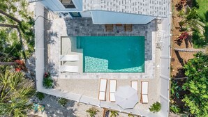 An aerial view of a modern house with a swimming pool, white lounge chairs, and a covered patio area. - 197 Beach Daze: 3br Pool Home, W/ Deeded Beach Access! 3 Bedroom Home (Fort Myers Beach)