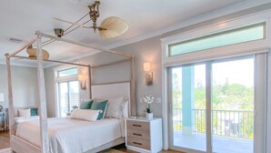 A four-poster bed with a canopy, a bedside table with drawers, a large window with a view of greenery, and a ceiling fan. - 135 Island Escape: 5br Home W/ Pool And Spa! 5 Bedroom Home (Fort Myers Beach)