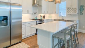 A modern kitchen with white cabinetry, stainless steel appliances, and a large island with bar stools. - 135 Island Escape: 5br Home W/ Pool And Spa! 5 Bedroom Home (Fort Myers Beach)