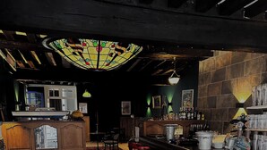 A bar area with a wooden counter, red bar stools, and a stained glass ceiling. - Chez Jacques-Louis (Cosne-Cours-sur-Loire)