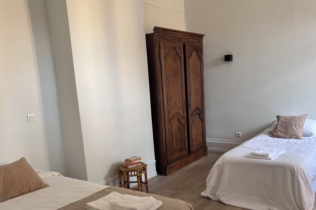 A hotel room with two beds, a wooden wardrobe, and a small table.