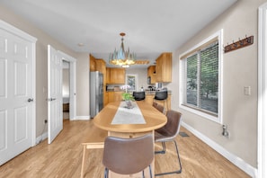 A modern kitchen with wooden cabinets, a central island with chairs, and a chandelier.