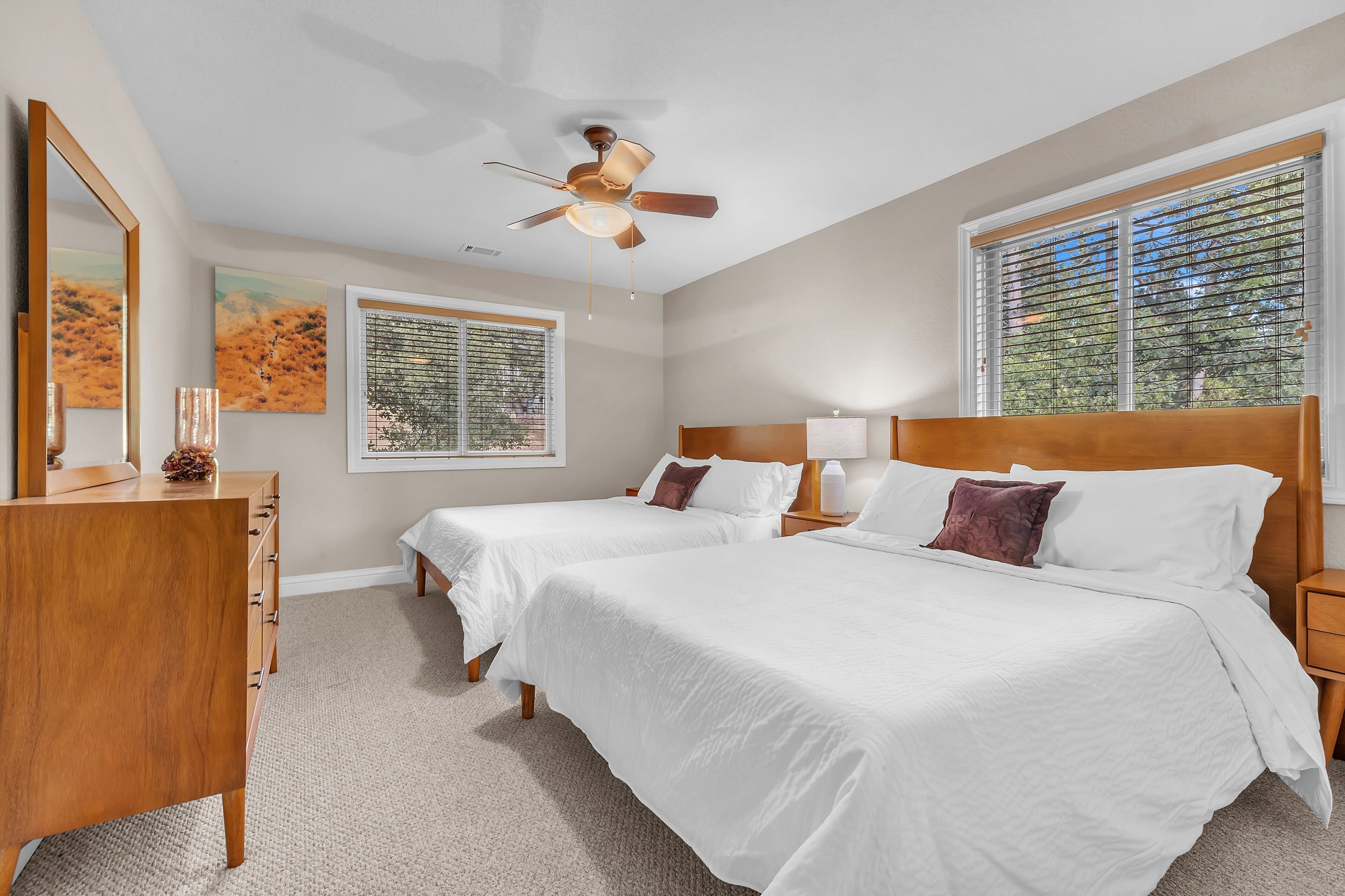 A bedroom with two beds, a ceiling fan, a dresser, and a window with blinds.