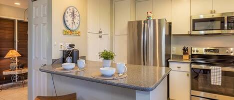 A modern kitchen with a central island, stainless steel appliances, and a clock on the wall.