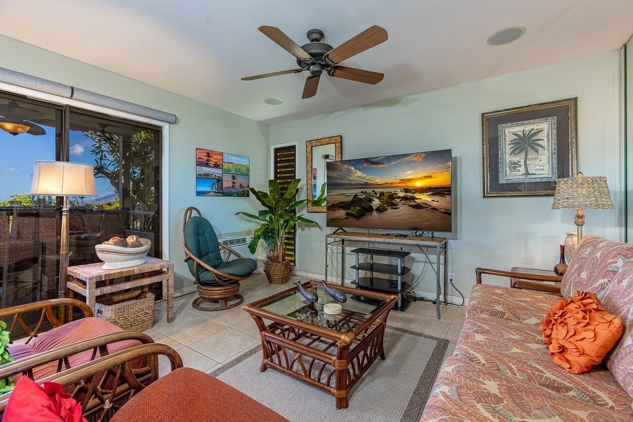 A living room with a ceiling fan, a television, wicker furniture, and a large window.