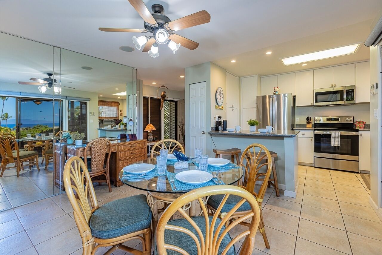 A modern kitchen with a central island, stainless steel appliances, and a dining area with wicker chairs and a glass table.