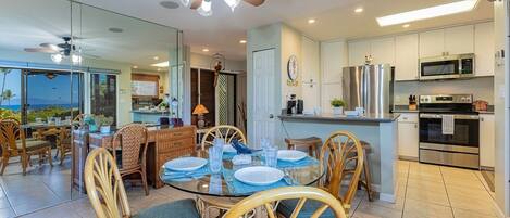 A modern kitchen with a central island, stainless steel appliances, and a dining area with wicker chairs and a glass table.