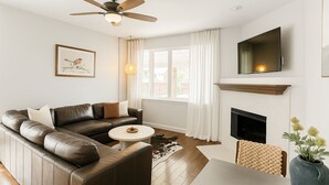A modern living room with a leather sofa, a round coffee table, a fireplace, and a ceiling fan.