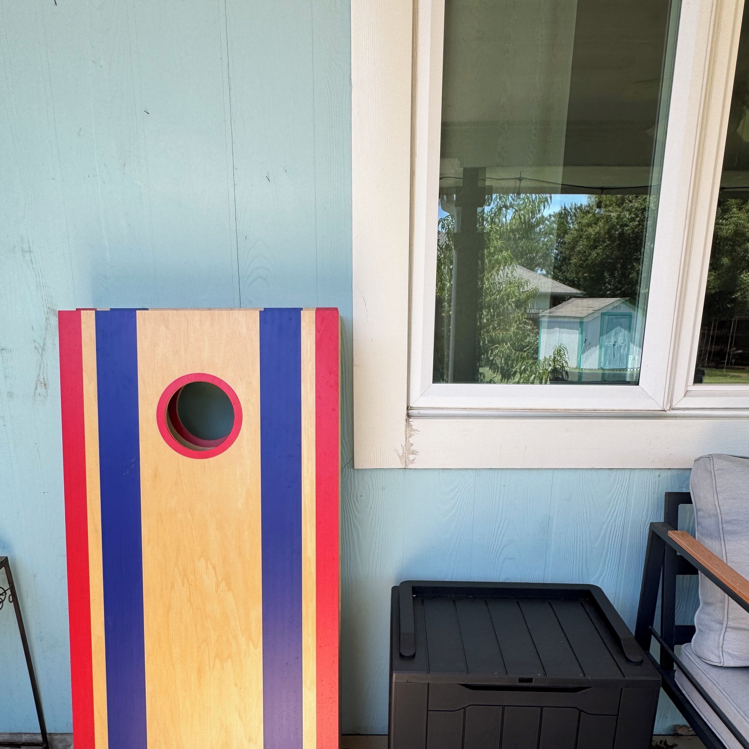 A colorful wooden board game with a hole in the center, placed next to a window with a view of a house and trees.