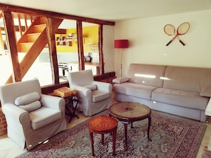 A living room with a sofa, two armchairs, a coffee table, a patterned rug, and a wall-mounted tennis racket decoration.