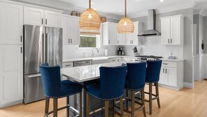 A modern kitchen with white cabinets, a stainless steel refrigerator, a gas stove, and blue bar stools.