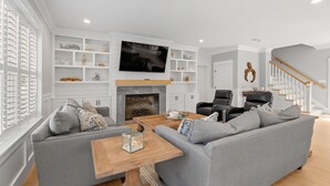 A modern living room with a fireplace, a flat-screen TV, and a staircase.