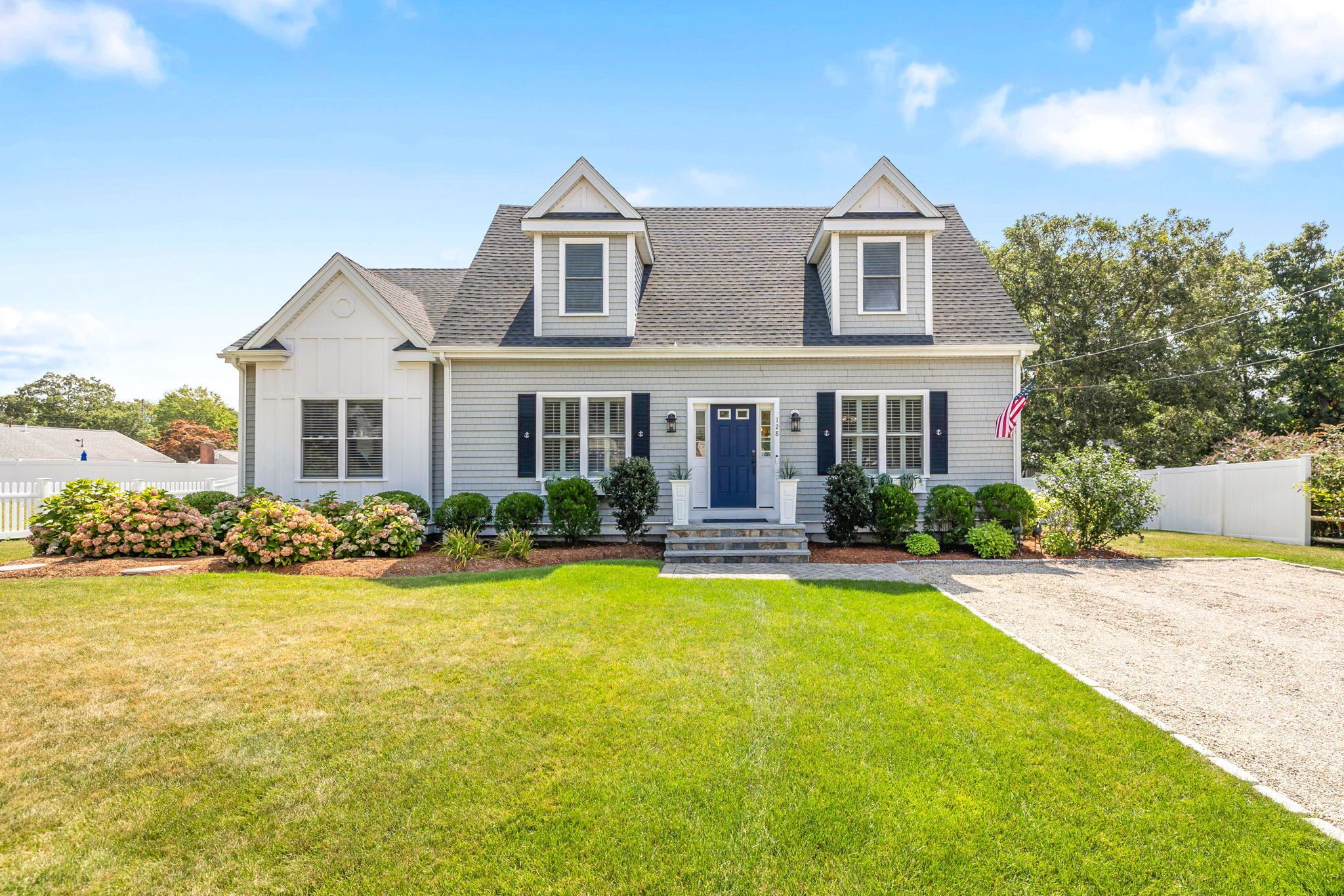 A two-story house with a front porch, a blue door, and a small front yard with a lawn and shrubs.