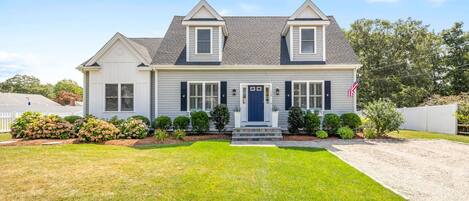 A two-story house with a front porch, a blue door, and a small front yard with a lawn and shrubs.