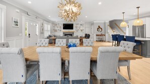 A modern kitchen with a built-in oven, a dining area with a wooden table and grey upholstered chairs, and a staircase leading to an upper level.