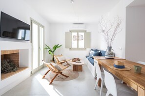 Un salon moderne doté d’un téléviseur à écran plat, d’une cheminée, de fauteuils en osier, d’une table à manger en bois et d’un canapé avec des coussins bleus.