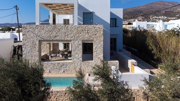 Une maison moderne à deux étages, dotée d’une façade en pierre, d’une piscine et offrant une vue sur une montagne.