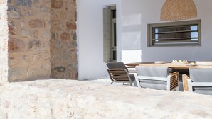 Un mur en pierre, une table en bois avec des chaises et une suspension lumineuse en fibres tressées.