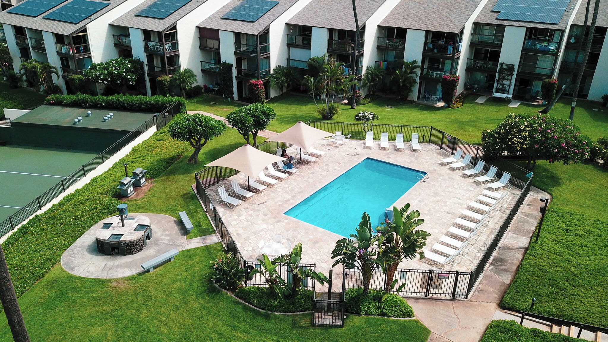 A rooftop pool surrounded by lounge chairs and a tennis court.