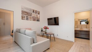 A modern living room with a sofa, a flat-screen TV, a small table with a vase of flowers, and a wall with cityscape photographs.