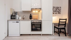 A compact kitchen with a dishwasher, microwave, stove, and a dining area with a chair.