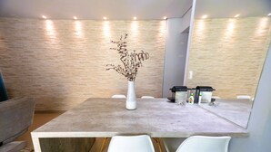 Un comedor moderno con una mesa de hormigón, sillas blancas y un jarrón con ramas secas.