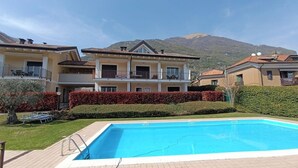 A two-story building with a swimming pool, surrounded by a well-maintained garden and a mountain in the background. - Duplex with pool, terrace and 2 bedroom (Lenno)