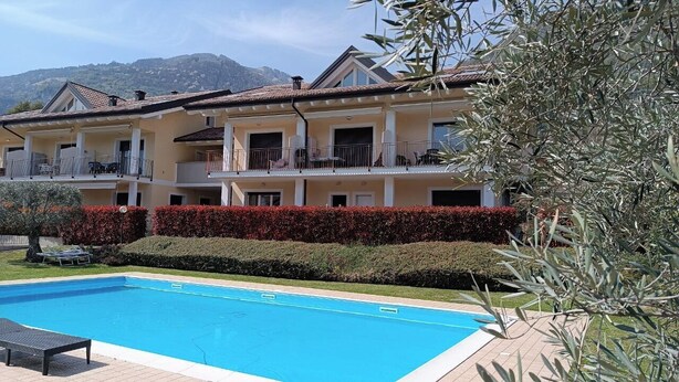 A multi-story hotel with a swimming pool, balconies, and a mountainous backdrop. - Duplex with pool, terrace and 2 bedroom (Lenno)