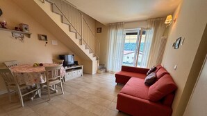 A living room with a staircase, a dining table with chairs, a red sofa, and a television. - Duplex with pool, terrace and 2 bedroom (Lenno)