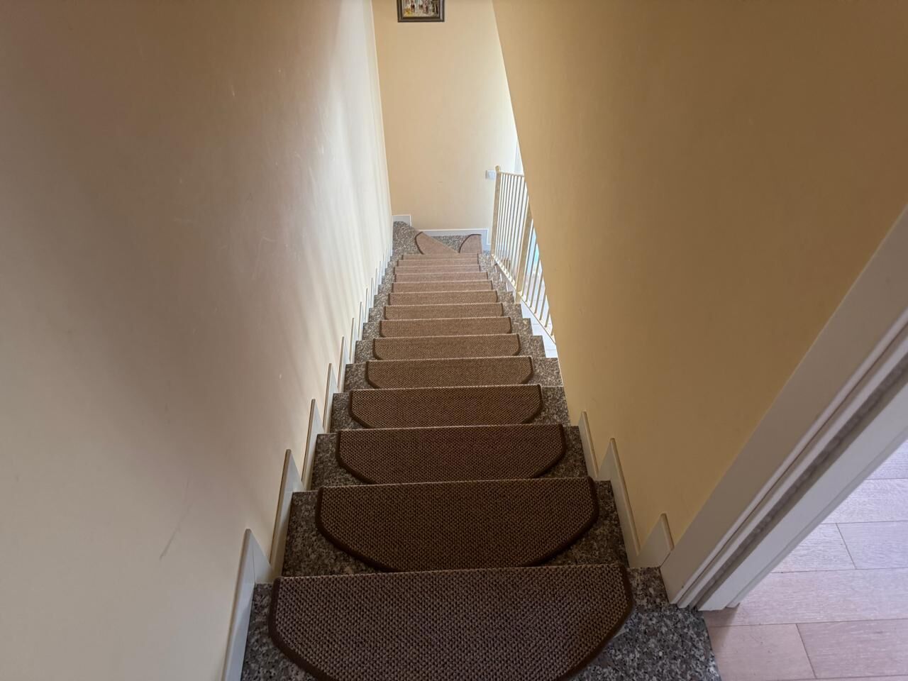 A carpeted staircase with a handrail, leading to a landing with a picture frame.