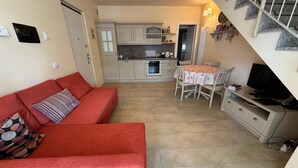 A living room with a red sofa, a dining table with chairs, a kitchen area, and a staircase. - Duplex with pool, terrace and 2 bedroom (Lenno)