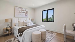 A bedroom with a large bed, two bedside tables, a window with a view, and a chair.