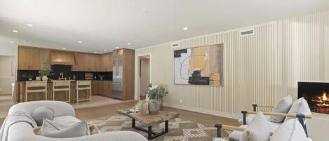 Una sala de estar moderna con chimenea, un comedor y una cocina con alacenas de madera y electrodomésticos de acero inoxidable.