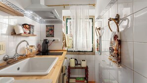 Una cocina con un lavamanos, hervidor, tostadora y ventana con cortina.